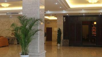 Vestíbulo con columnas de mármol, una mesa de recepción y una planta grande en maceta.