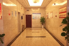 Um hall de hotel com piso de mármore, balcão de recepção, planta em vaso e cartazes informativos nas paredes.