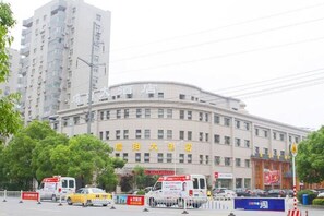 A large building with multiple floors and a curved facade, surrounded by trees and parked vehicles. - Ruipo Hotel (Xiantao)