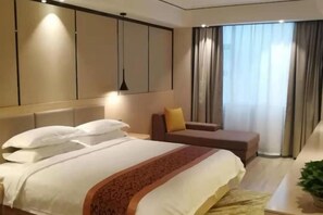 A hotel room with a bed, a seating area, a large window with curtains, and a pendant light.