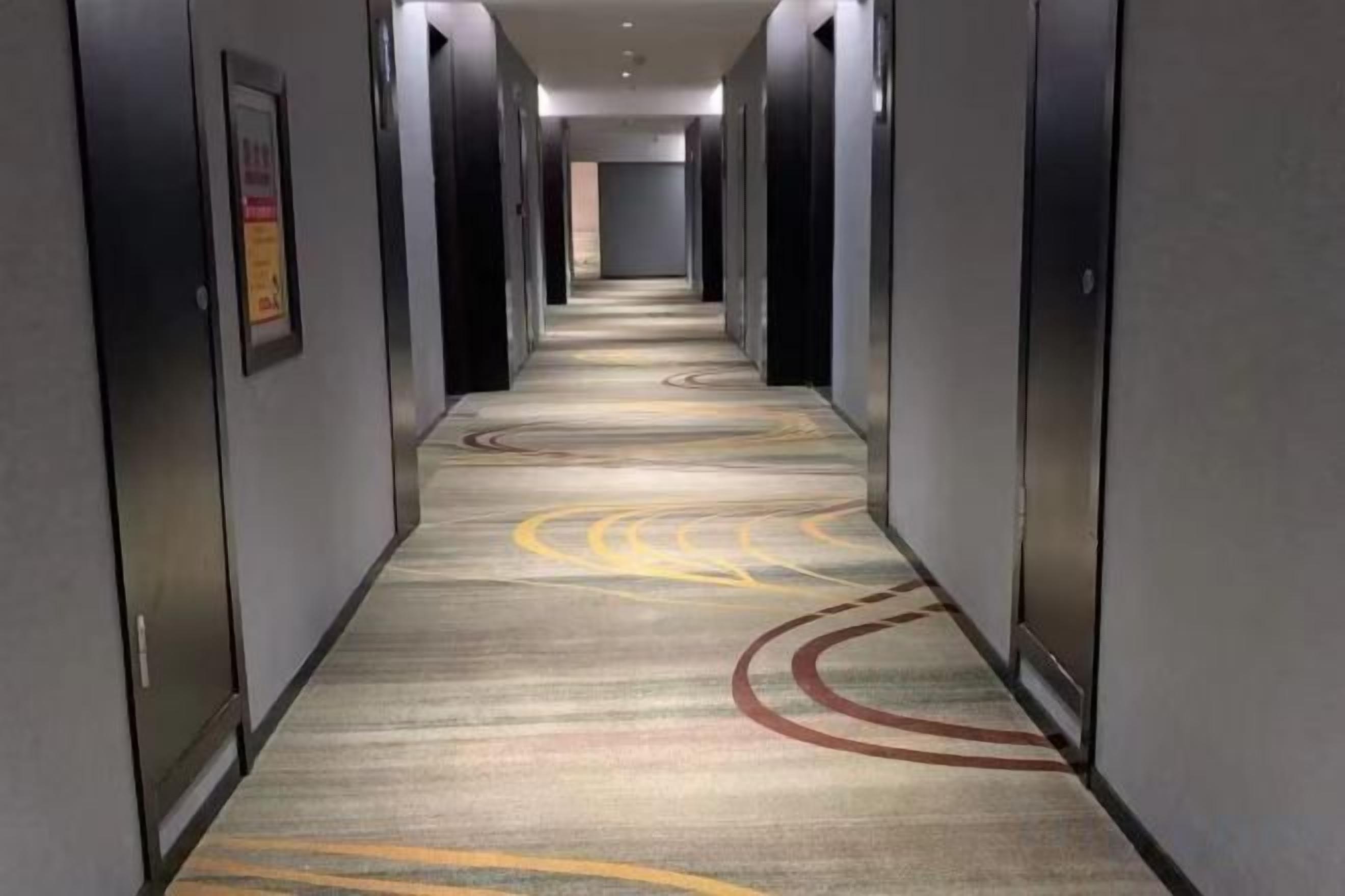 Un couloir d’hôtel avec un revêtement de sol en moquette et des portes de chaque côté.
