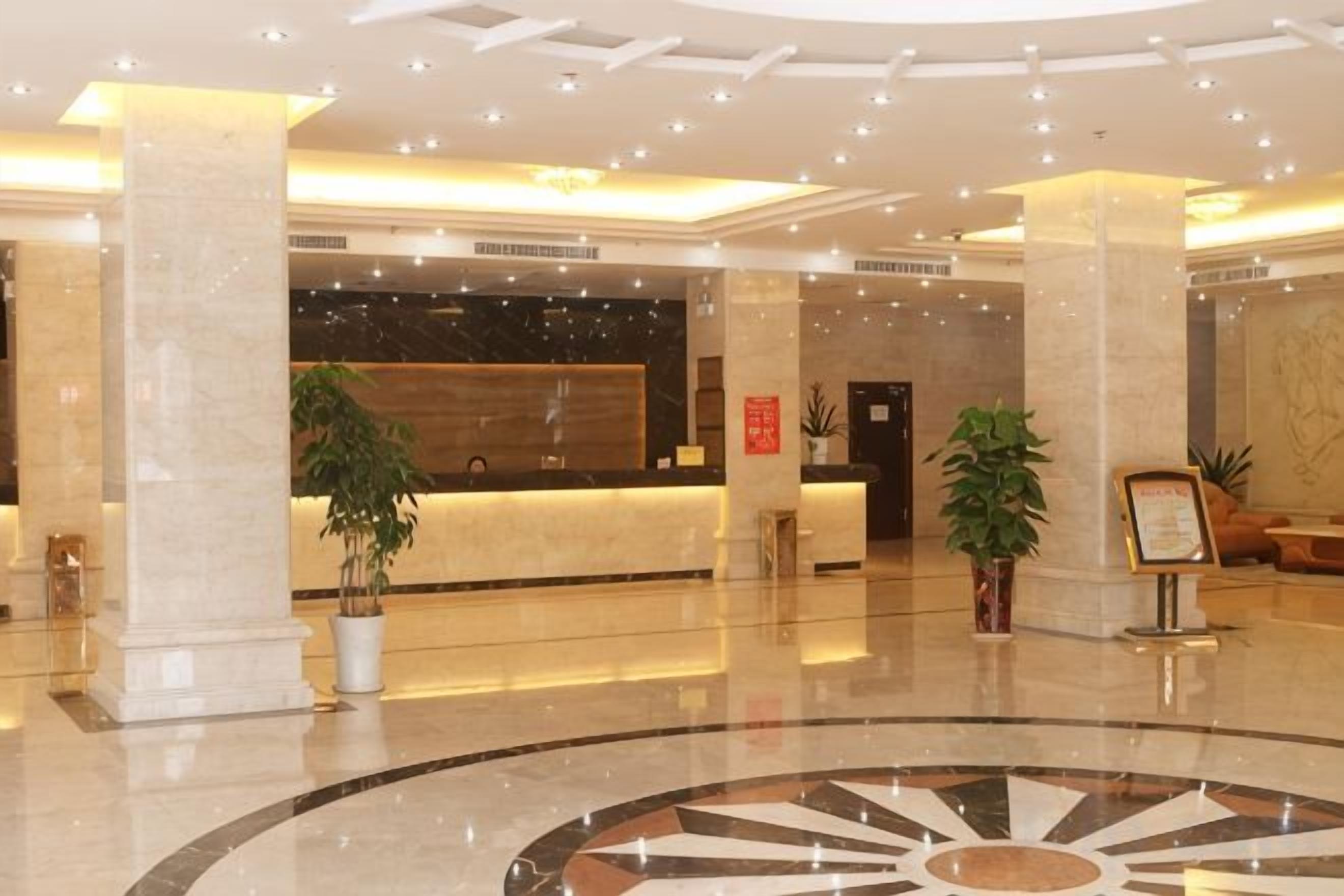 A hotel lobby with a reception desk, columns, and a circular floor design.
