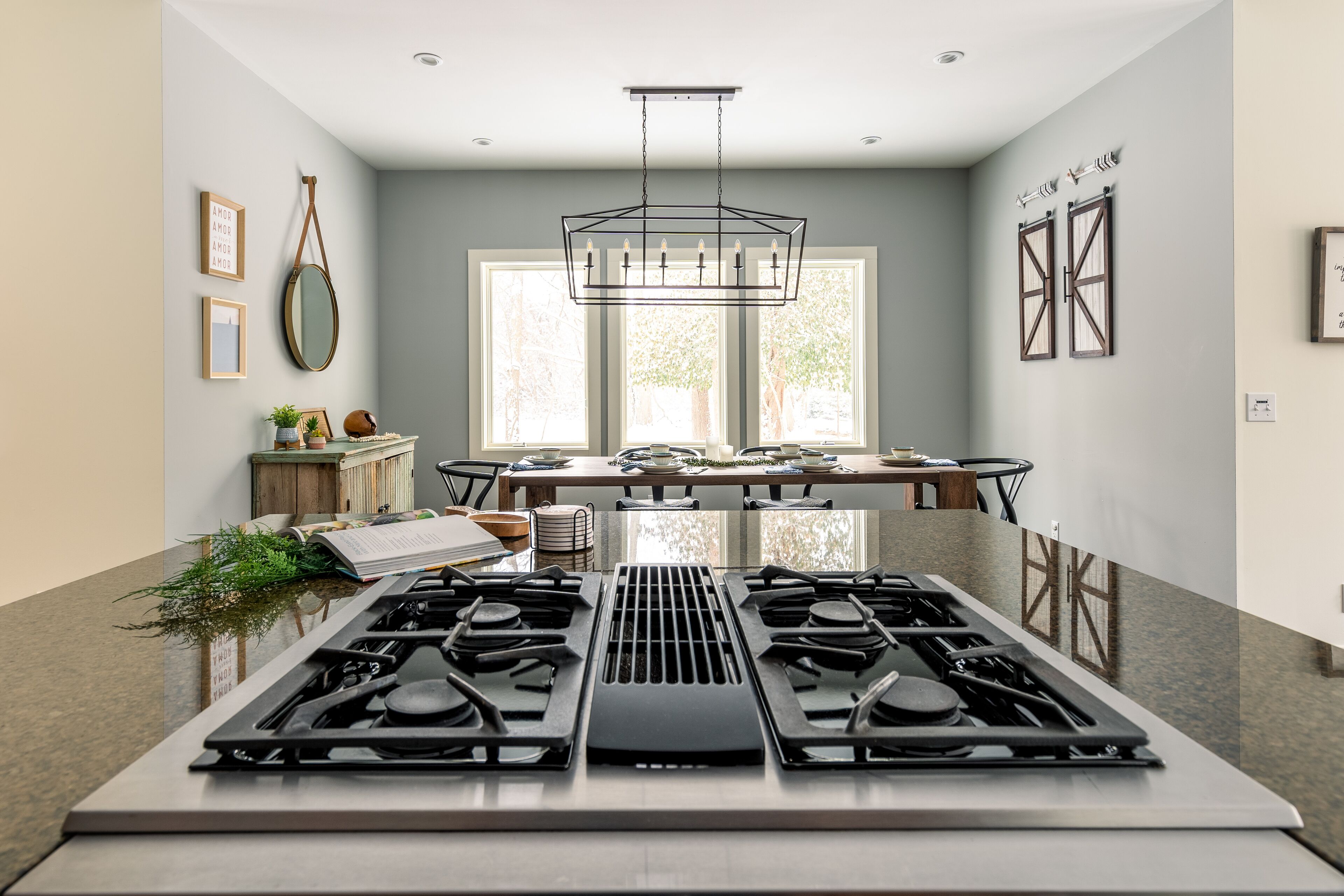 Una cucina moderna con piano cottura a gas centrale, ampie finestre e zona pranzo con tavolo e sedie.