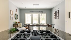 A modern kitchen with a central gas stove, large windows, and a dining area with a table and chairs.