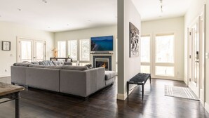 A modern living room with a gray sectional sofa, a fireplace, and a large TV on the wall.