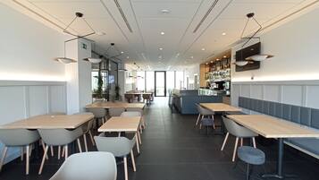 A modern restaurant with multiple dining tables and chairs, a bar area, and a television screen.