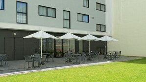 Een terras met tafels, stoelen en parasols, met een gevel op de achtergrond.