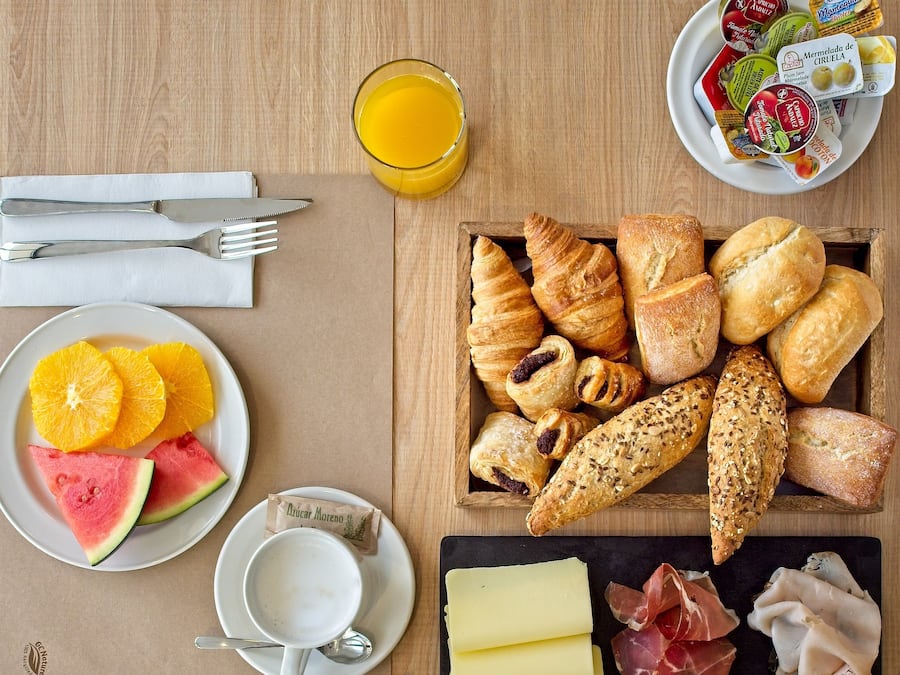 Desayuno con cruasanes, pan, queso, prosciutto, sandía, gajos de naranja y jugo.