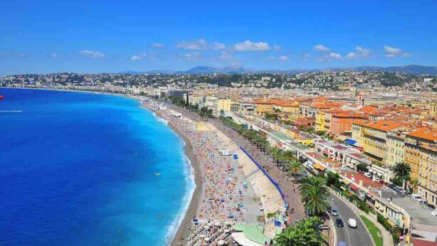 Paisagem costeira com praia, edifícios e céu azul claro.