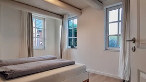 Ein Schlafzimmer mit einem Bett, zwei Fenstern und einer Tür.