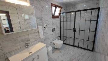 A bathroom with a marble floor, a white sink, a toilet, and a glass-enclosed shower area.