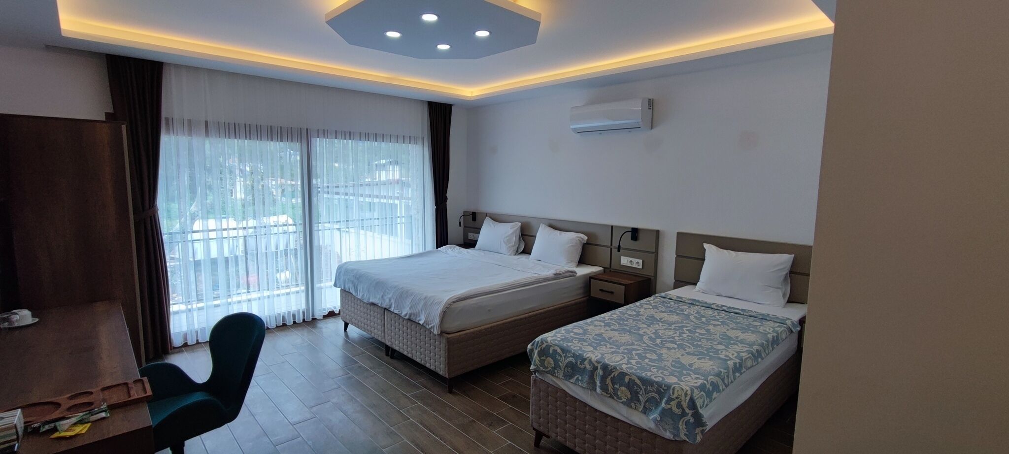 A hotel room with two beds, a desk, a chair, and a large window with curtains.