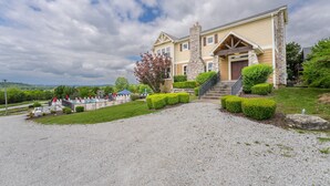 Una casa a due piani con un camino in pietra, un portico e un vialetto sterrato.