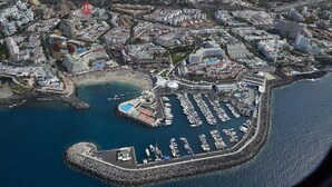 An aerial view of a coastal city with a marina, residential buildings, and a large hotel with a distinctive dome structure. - Comfortable, quiet apartment close to everything (Costa Adeje)