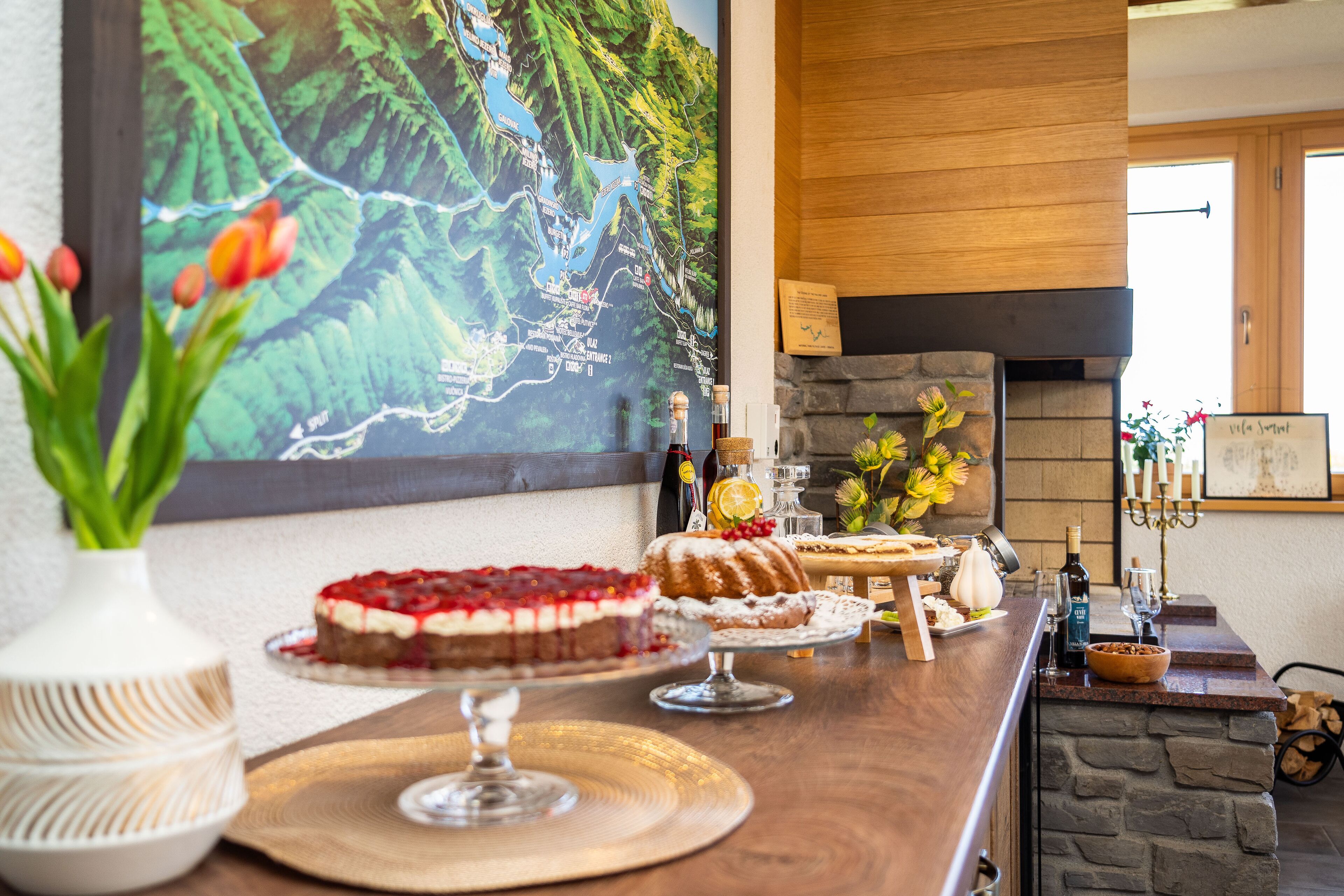 A bar area with a stone fireplace, a map on the wall, and various desserts on display.