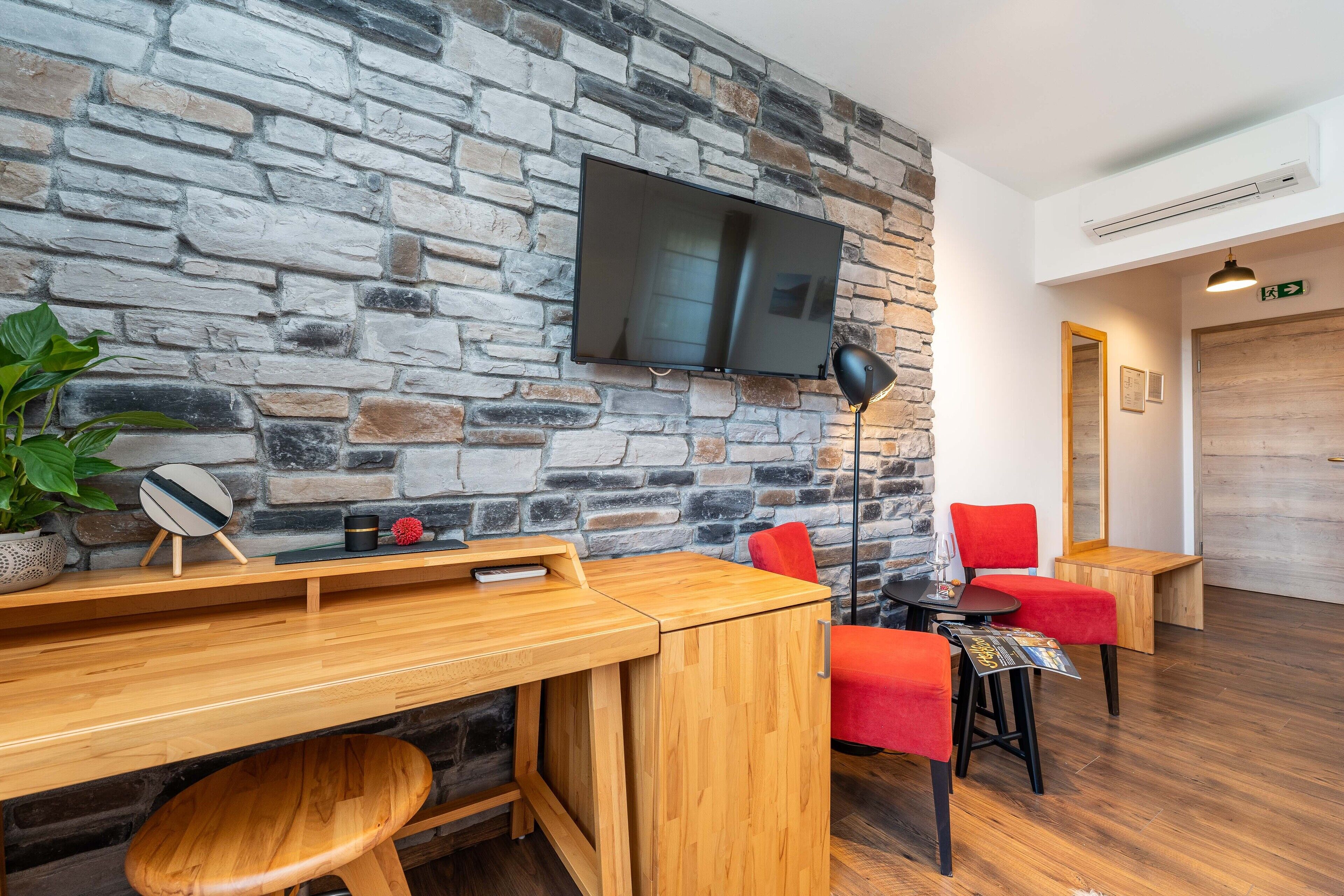 Una habitación moderna con pared de piedra, televisor de pantalla plana, muebles de madera y una silla roja.