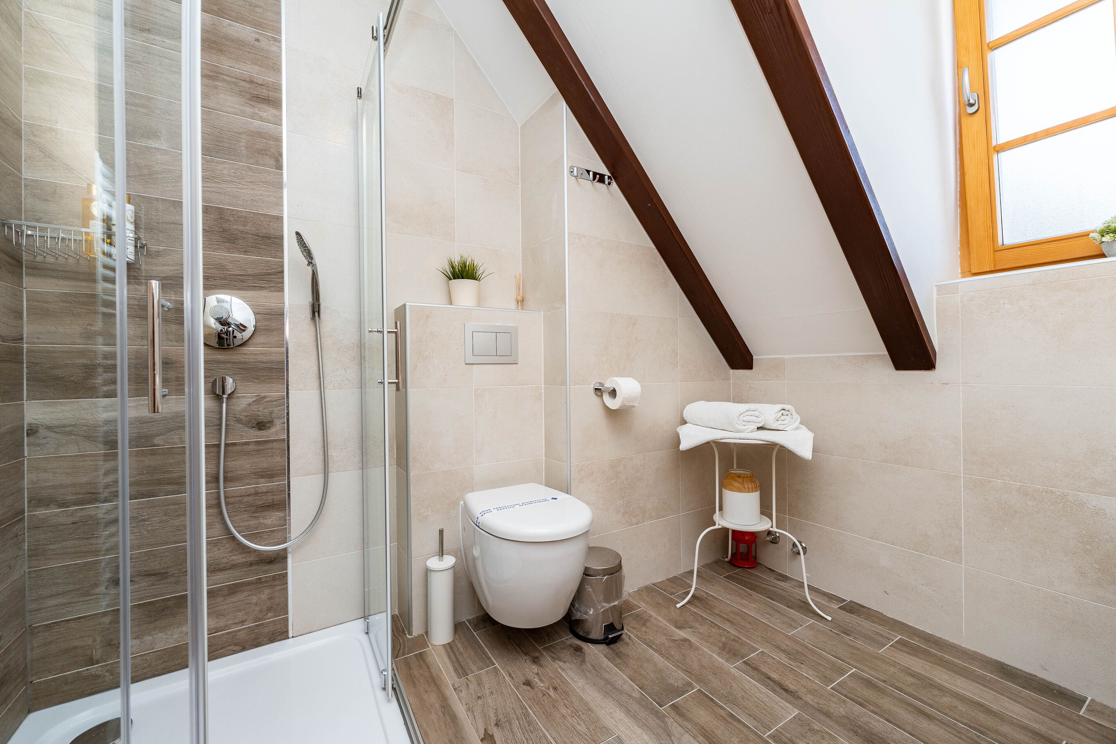Ein modernes Badezimmer mit Dusche, Toilette und Waschbecken, mit Holzboden und schrägverdeckelter Decke.