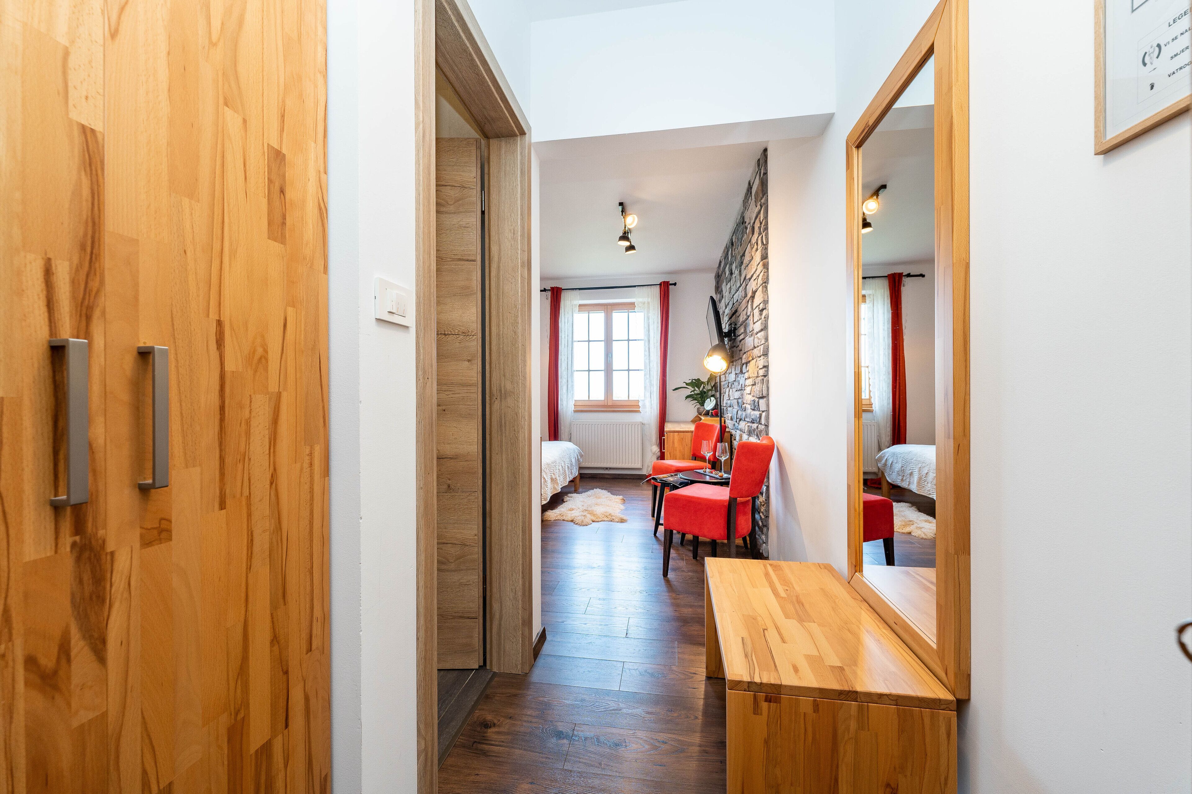 A hallway leading to a bedroom with a wooden door, a dining area with a table and chairs, and a large mirror on the wall.
