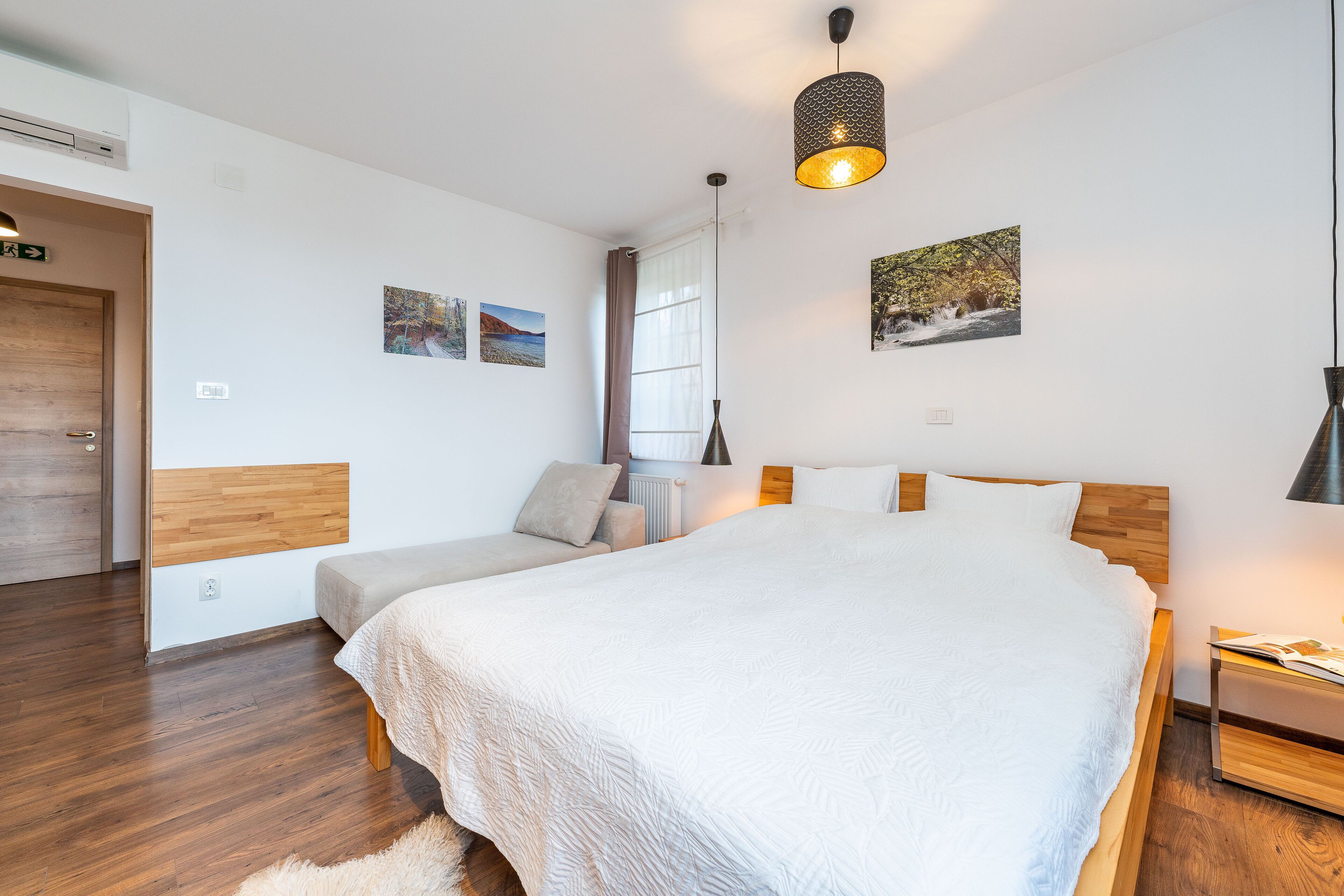 Une chambre à coucher avec un grand lit, une table de chevet, une commode, une tête de lit en bois et une fenêtre avec des rideaux.