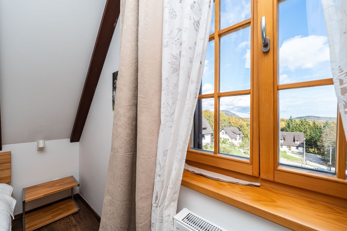 A bedroom with a wooden bed, a window with a view of houses, and a radiator.