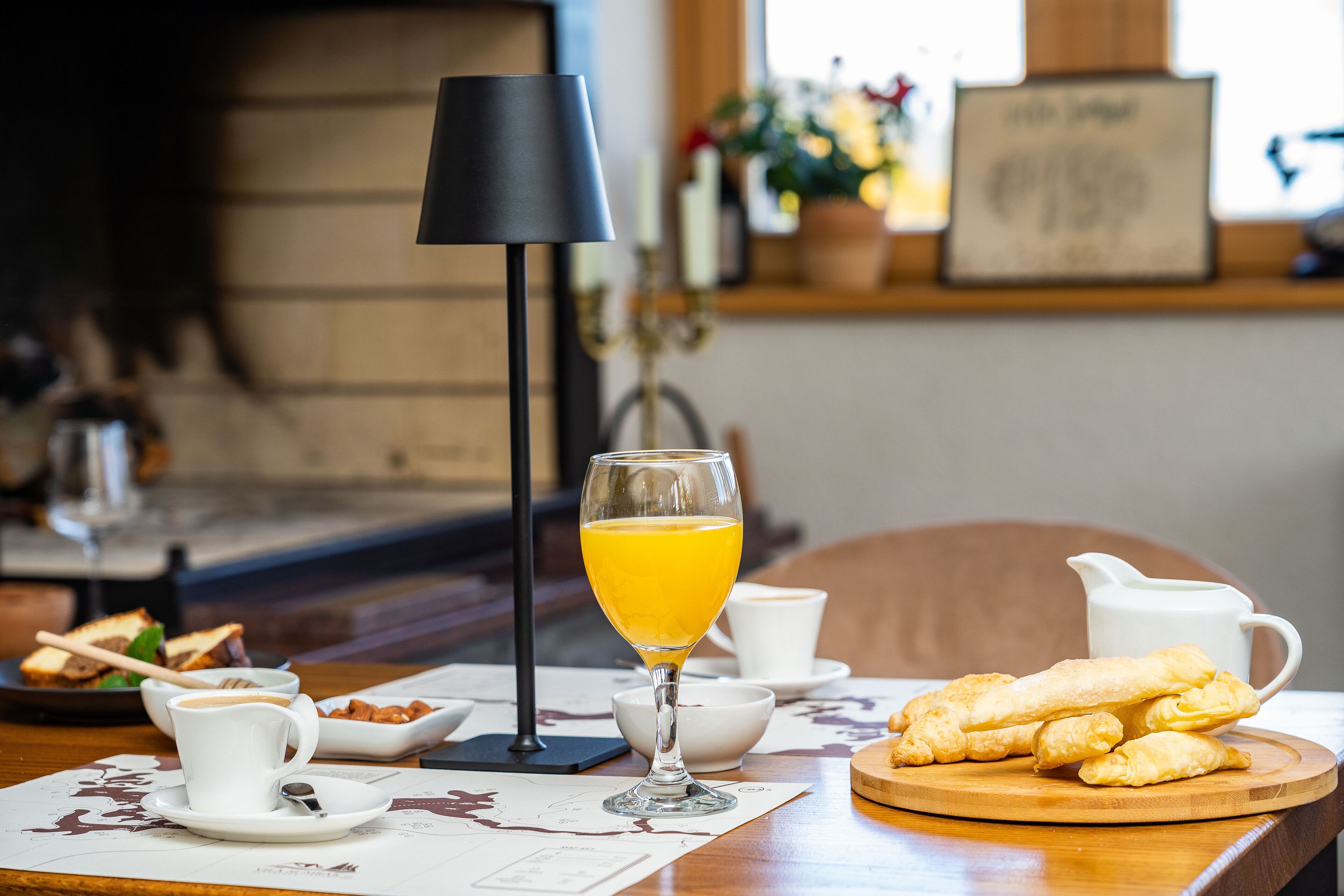Ett frukostbord med ett glas apelsinjuice, en kopp kaffe, croissanter och en mjölkkanna.