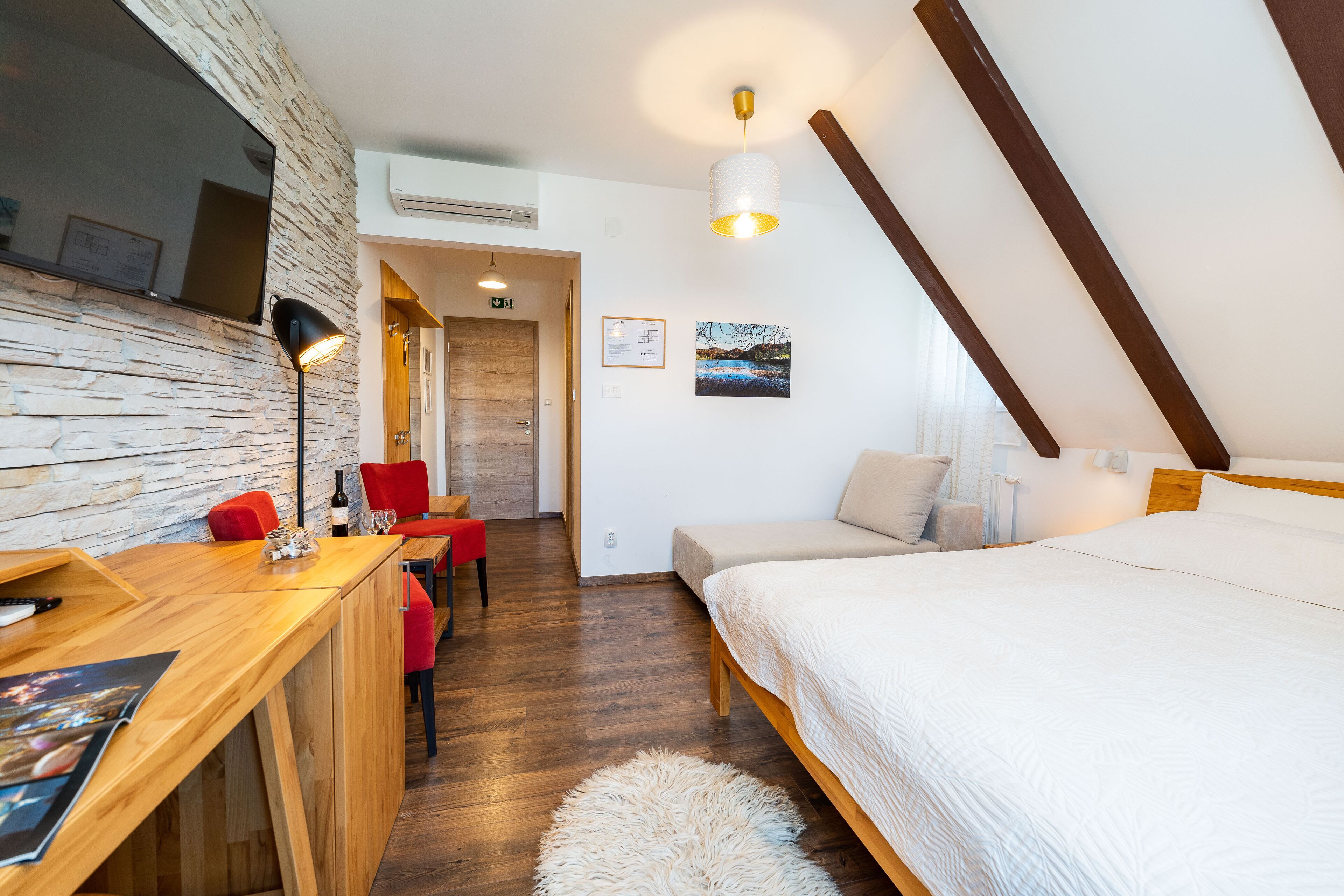 A modern room with a wooden desk, a bed, a red chair, and a white furry rug.