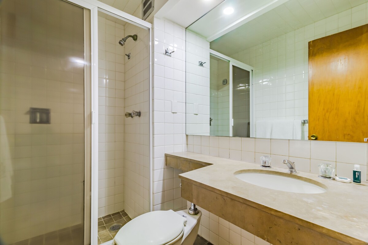 A bathroom with a shower, toilet, sink, and mirror.