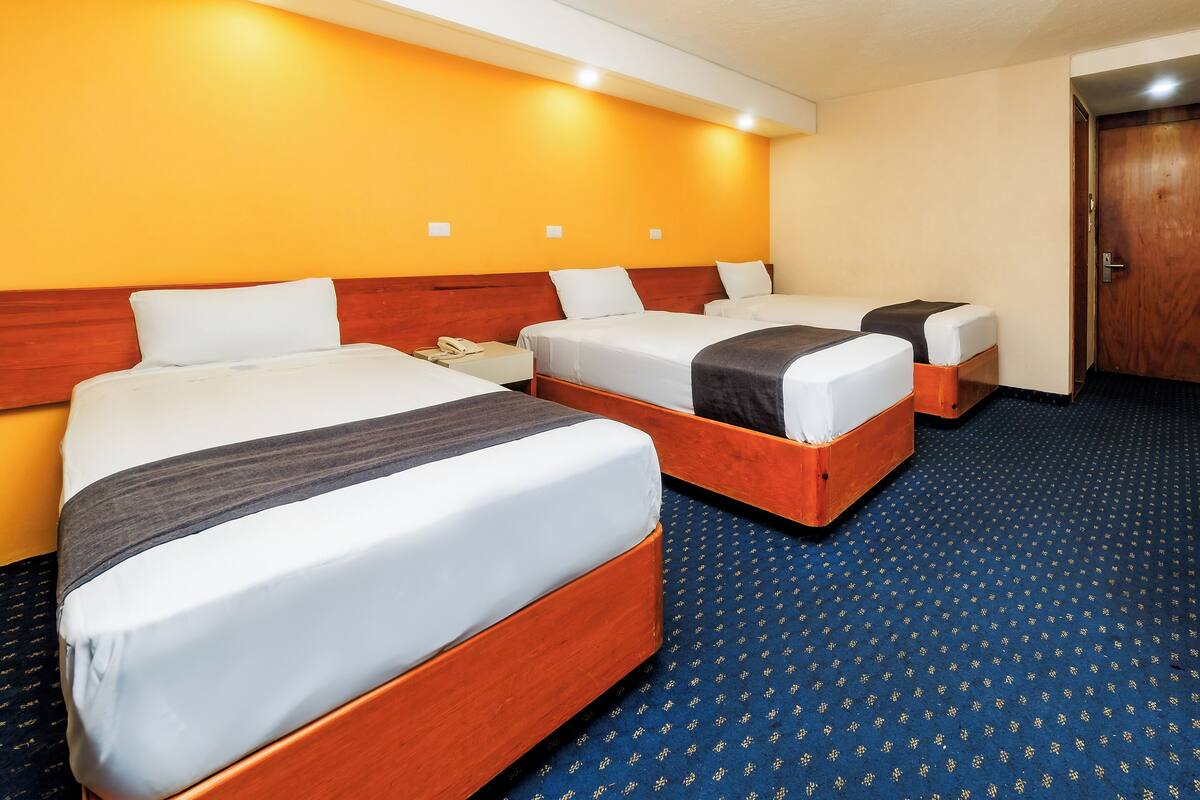 Una habitación de hotel con tres camas, un cabecero de madera y una alfombra azul.