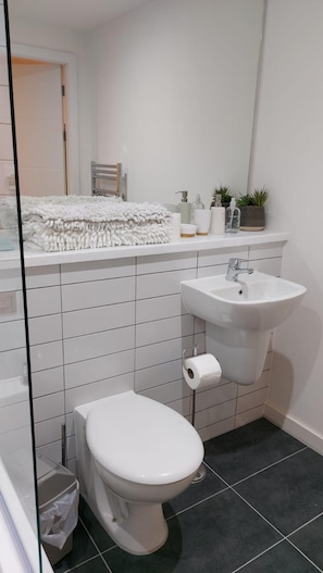 A modern bathroom with a white toilet, a sink, and a mirror. There is a towel rack with a white towel and a small potted plant on the counter. - Charming 1-bed Villa in Liverpool (Liverpool)