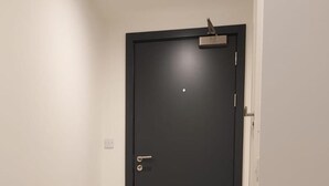 Ein Flur mit einer dunklen Tür, hellen Wänden und einem grauen Teppich auf dem Boden.