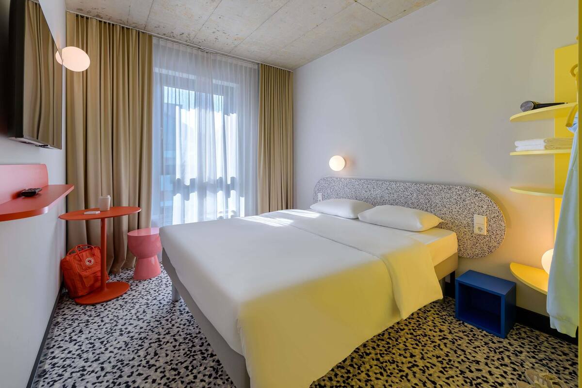 A hotel room with a bed, a TV, a small table, and a chair.