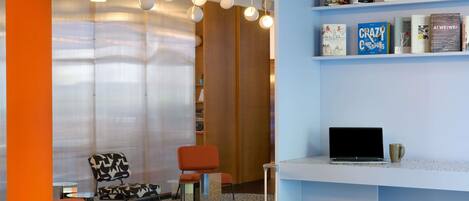 Un área de descanso moderna con una computadora portátil sobre una encimera, una estantería con libros y una zona de estar con sillas y un tapete estampado.