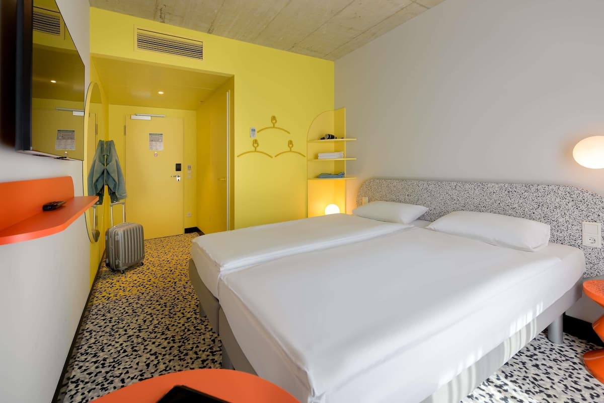 Een hotelkamer met een bed, een bureau, een stoel, een kapstok en een koffer.