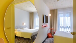 Een hotelkamer met een bed, bureau, stoel, televisie en spiegel.
