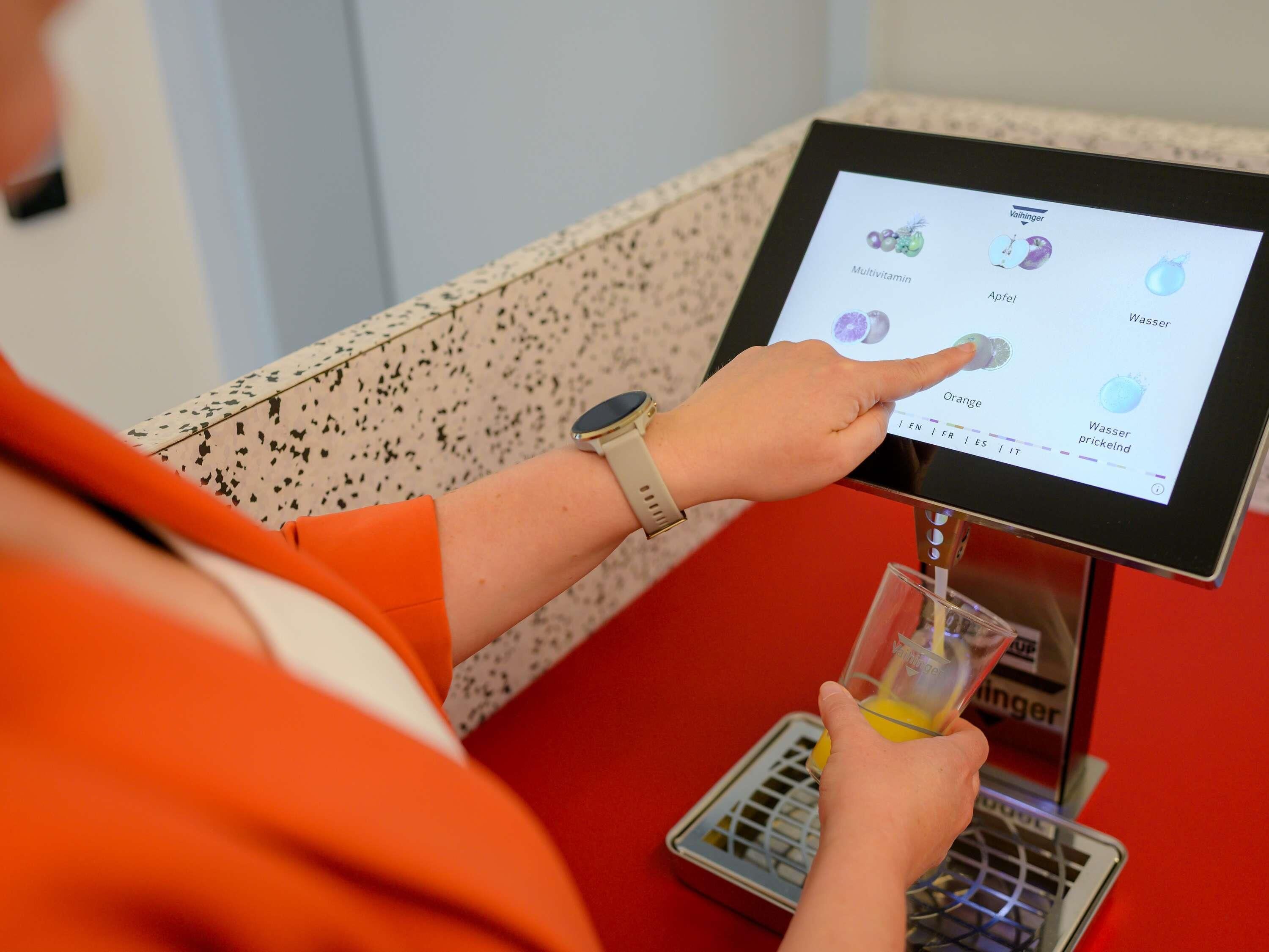 A person using a touchscreen device at a counter with a glass of orange juice.
