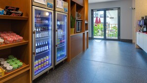Een gang met automaten, een koffieapparaat en uitzicht op een terras.