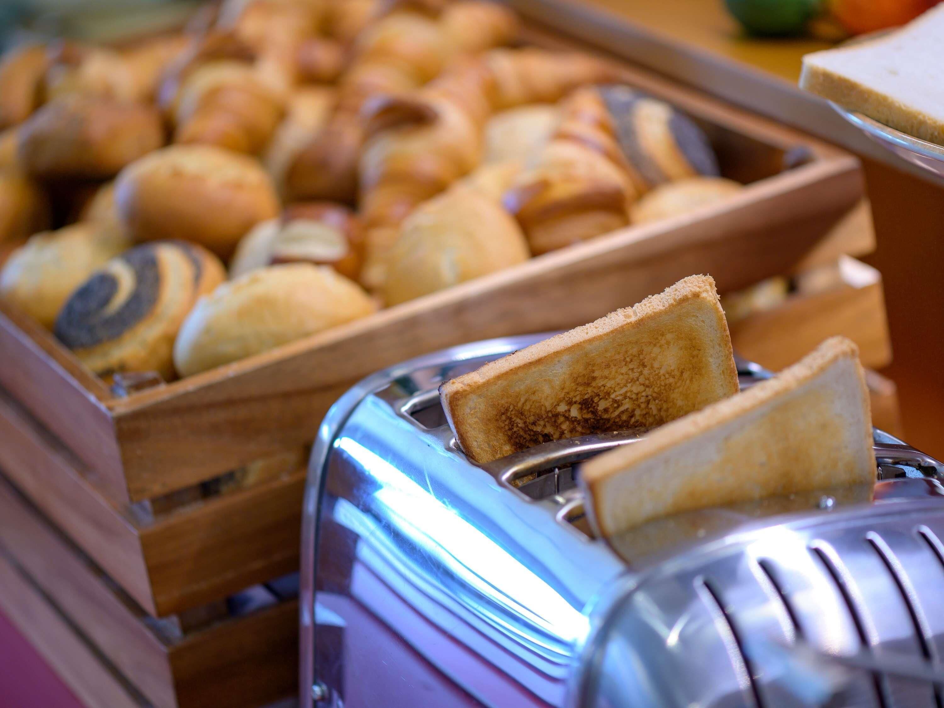 Ein Toaster mit einer Scheibe Brot darin und eine Auswahl an Gebäck im Hintergrund.