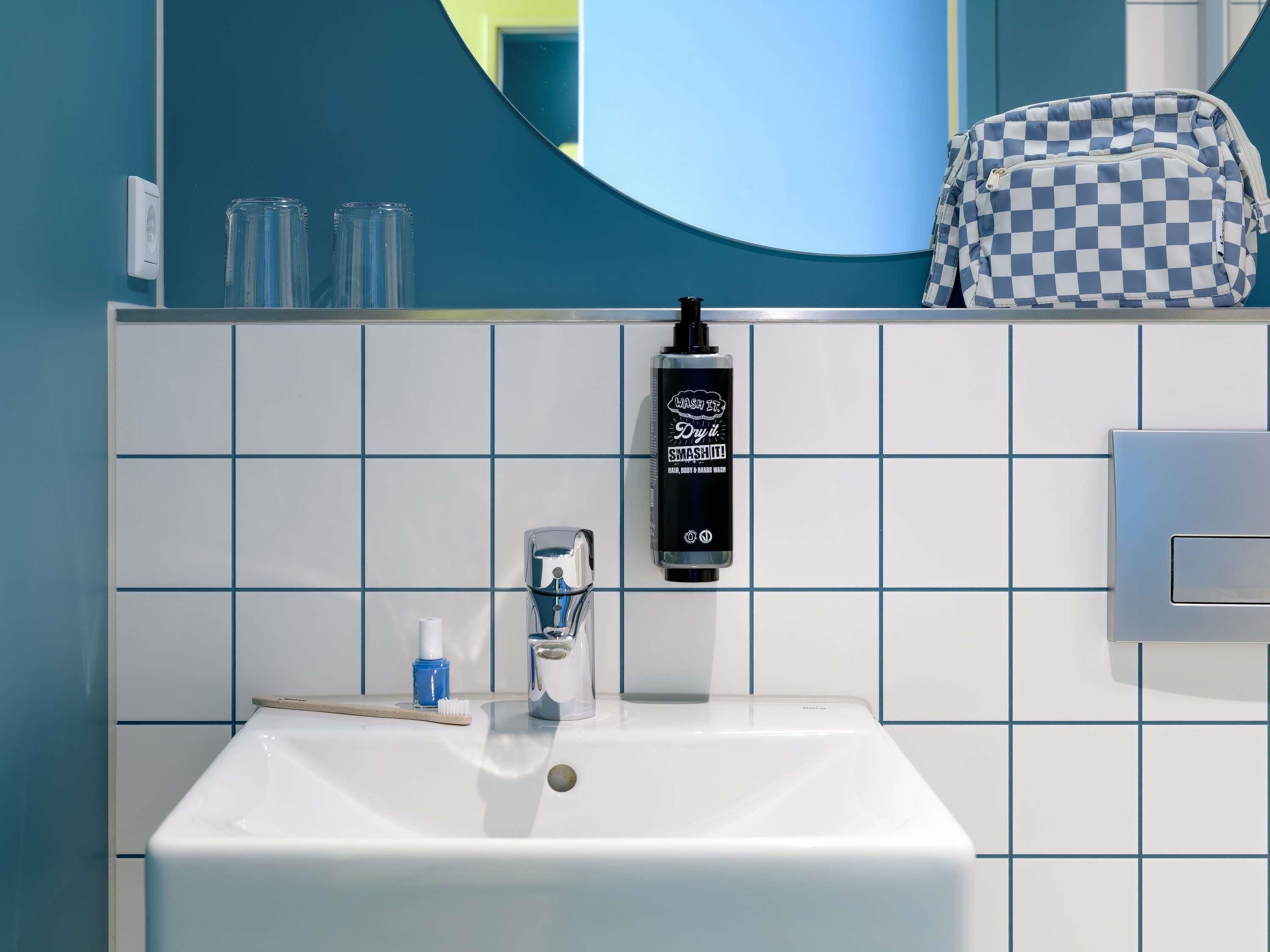 A bathroom with a white sink, a mirror, a soap dispenser, and a toothbrush.