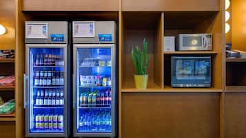 Dos máquinas expendedoras de bebidas, una planta en maceta y un microondas en un estante.