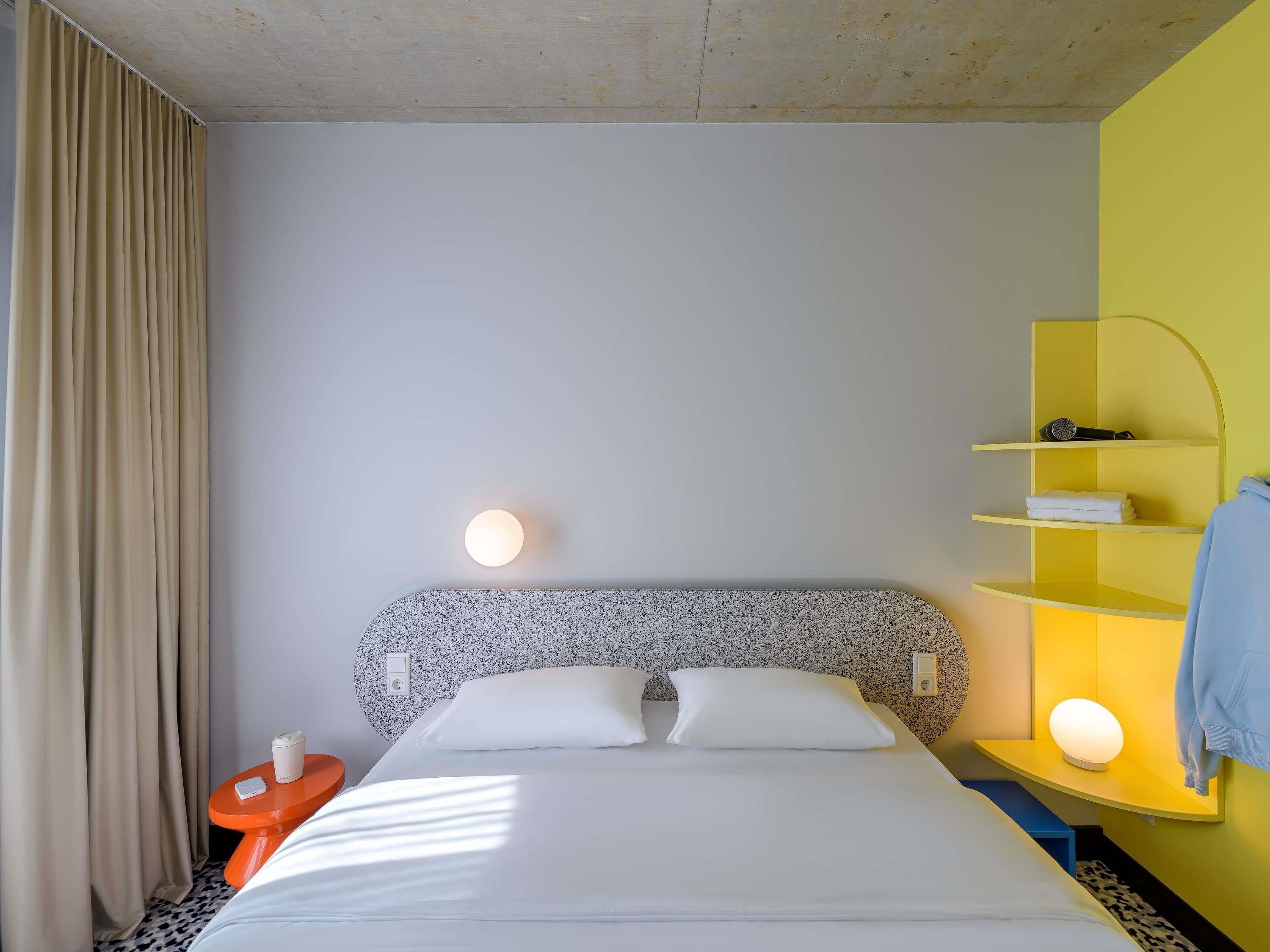 A hotel room with a bed, a nightstand, a lamp, and a shelf with a towel.