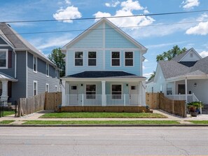 A two-story residential building with a front porch, a wooden fence, and a well-maintained lawn. - The Birch at Fountain SQ-King Bed INDY w/Fire Pit (Indianapolis)