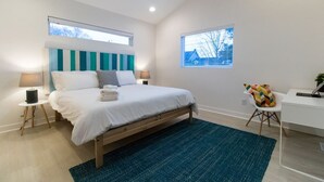 Een moderne slaapkamer met een bed, twee nachtkastjes, een bureau, een stoel en een plafondventilator.