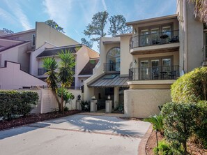 Un immeuble résidentiel moderne à plusieurs étages, doté d’un patio couvert, d’un petit jardin et d’une allée bien entretenue.