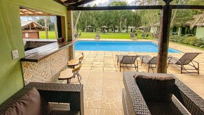 An outdoor pool area with a covered patio, lounge chairs, and a view of the pool. - QUATRO ESTAÇOES PESQ. E HOTEL FAZENDA (Esmeraldas)