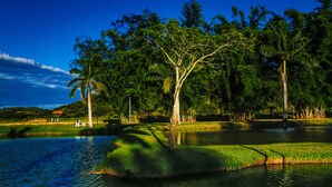 A serene landscape with a pond, trees, and a small building in the background. - QUATRO ESTAÇOES PESQ. E HOTEL FAZENDA (Esmeraldas)