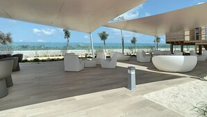 Un área de estar moderna al aire libre con mobiliario blanco, una terraza de madera y vista al mar.