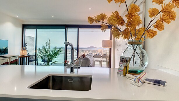 Una cocina moderna con un ventanal amplio, un lavamanos y un florero con flores amarillas.