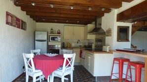A compact kitchen with a dining area, featuring a tiled floor, wooden ceiling beams, and basic appliances.