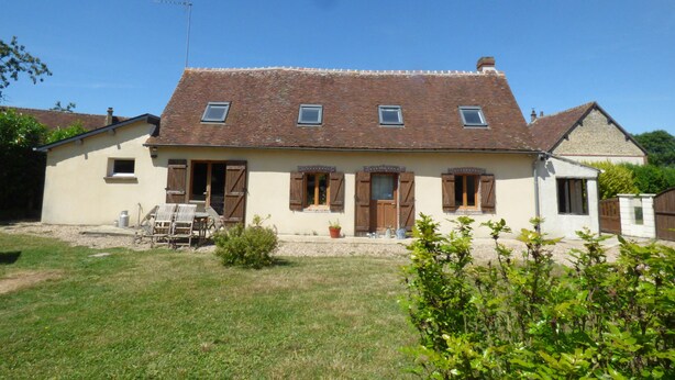 A two-story house with a tiled roof, multiple windows, and a small garden area in front.