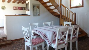 A dining area with a wooden staircase, white chairs, and a tiled floor.